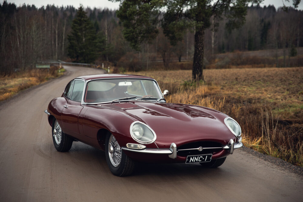 Vintage maroon Jaguar E-Type on a forest road