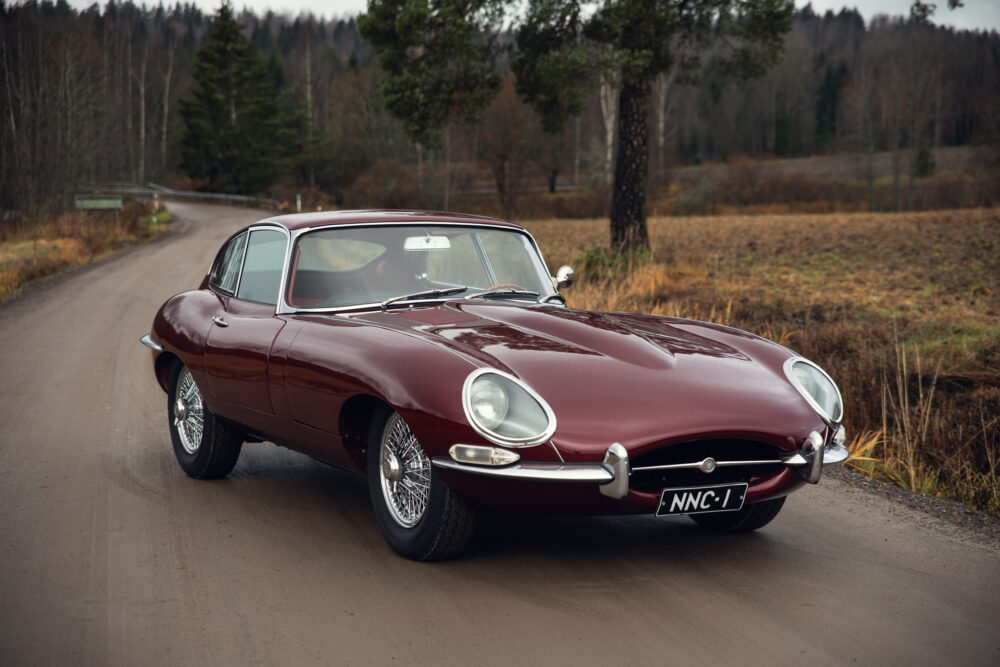 Vintage maroon Jaguar E-Type on forest-lined road