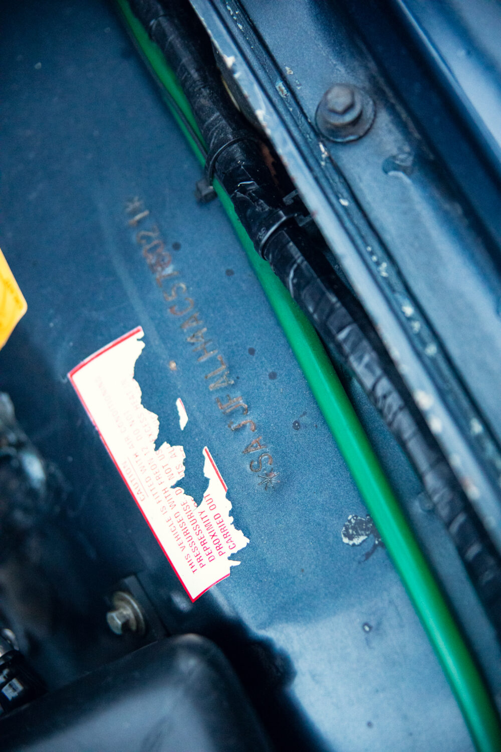 Car hood with worn warning label and cables