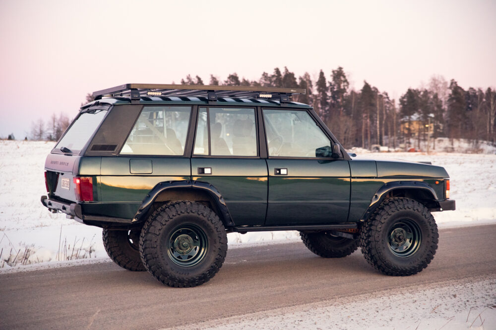 Green Range Rover on snowy road at dusk.