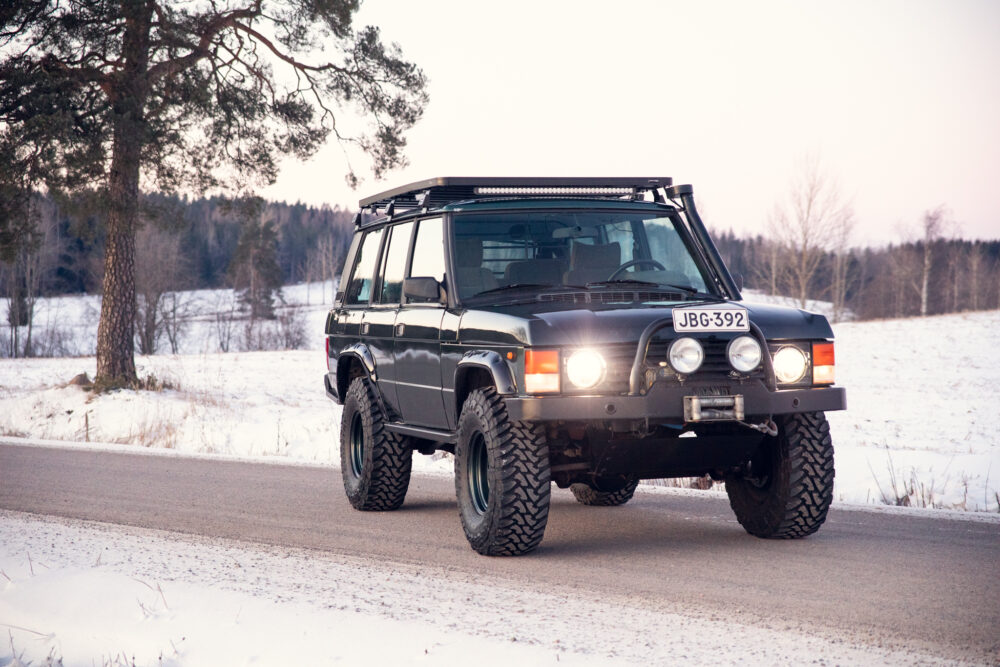 Modified SUV driving on snowy road near trees