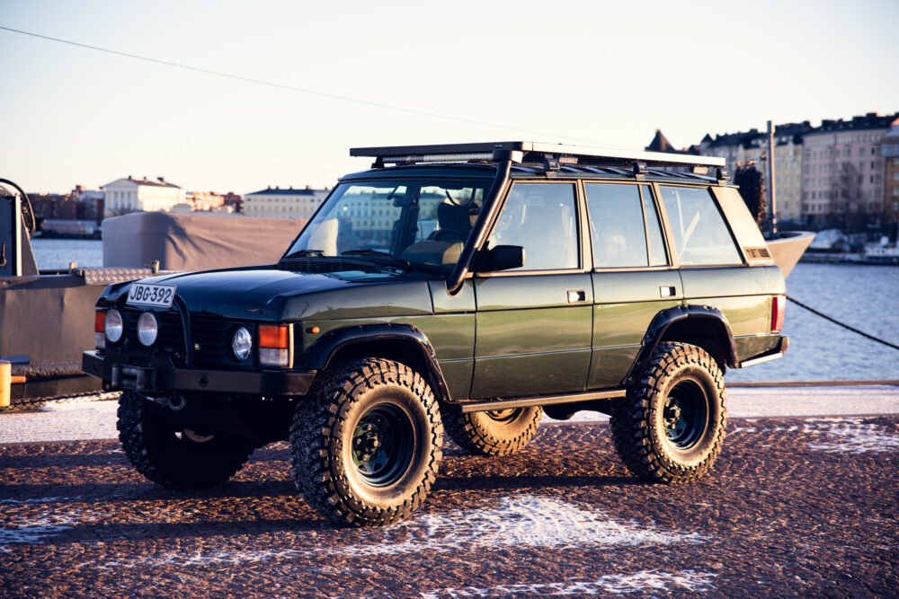 Green off-road vehicle parked by water at sunset