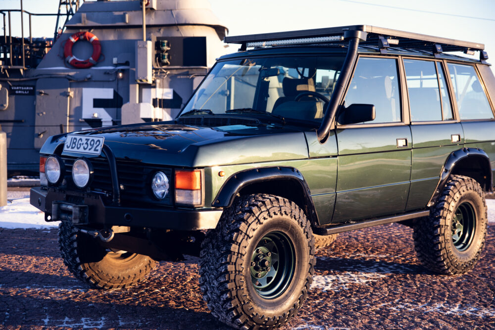 Green off-road SUV near navy ship at sunset
