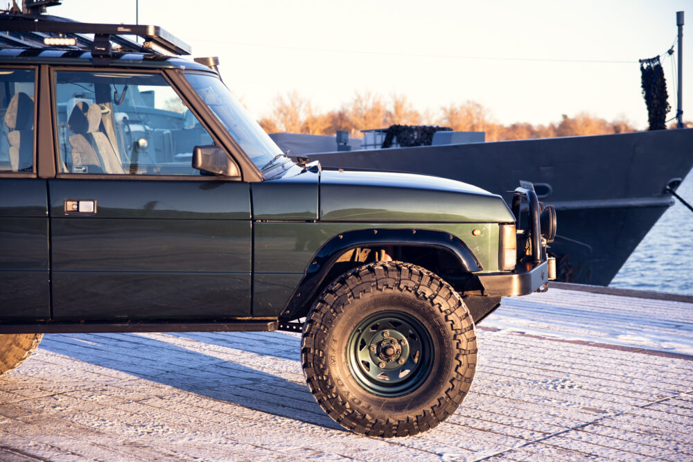 Green off-road vehicle parked by a ship at sunset
