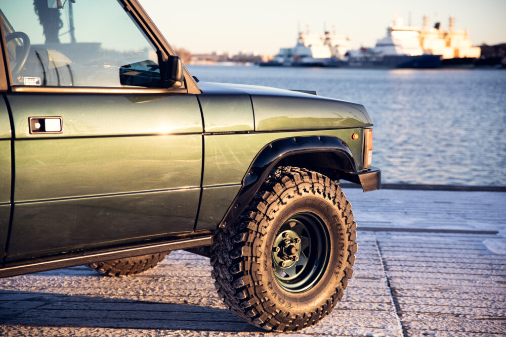 Green SUV on dock with ships in background