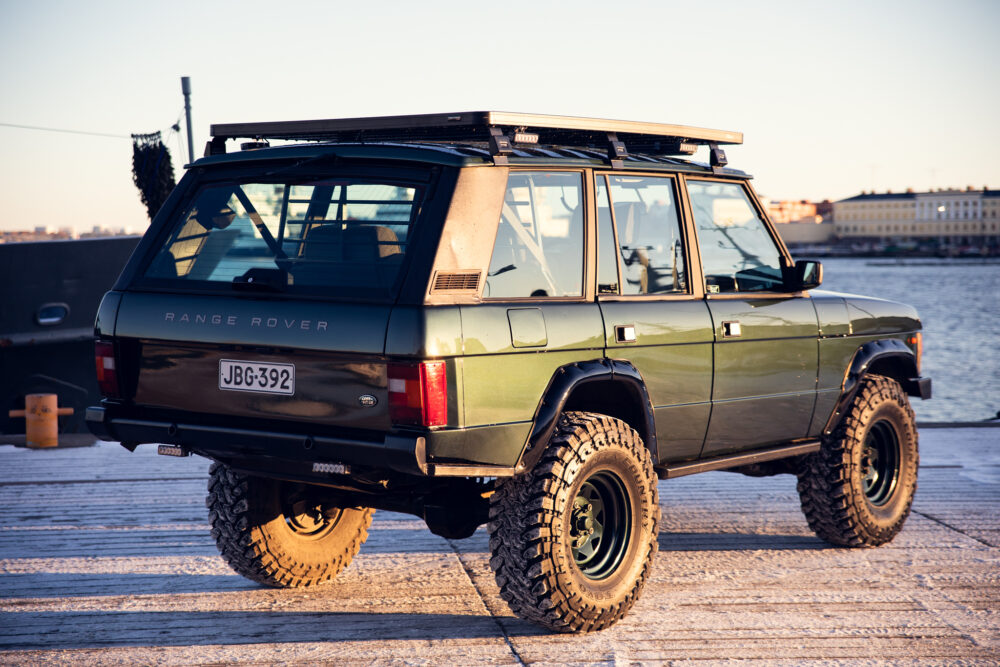 Vintage Range Rover parked on pier at sunset.