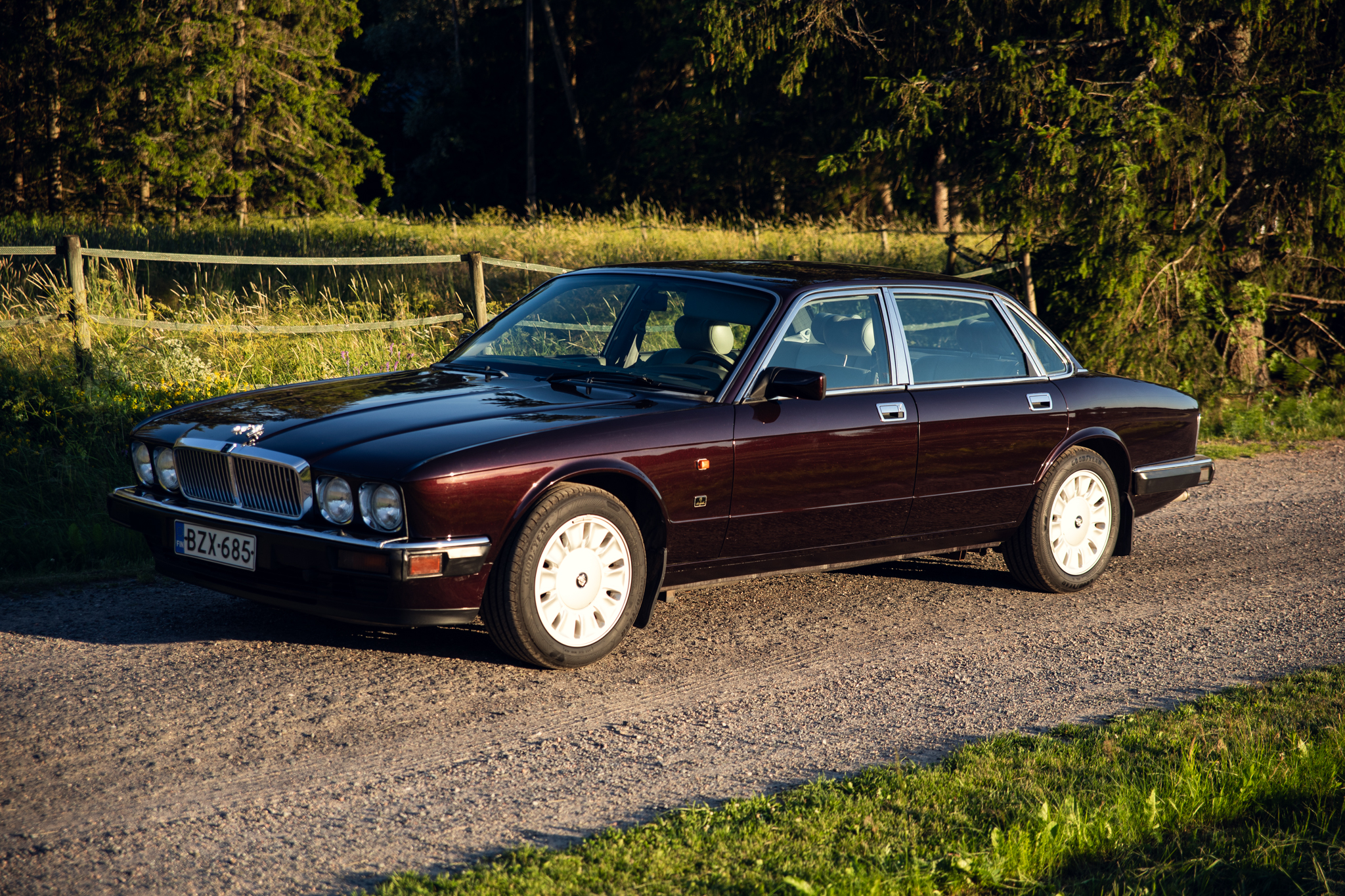 Classic burgundy luxury sedan parked on gravel road